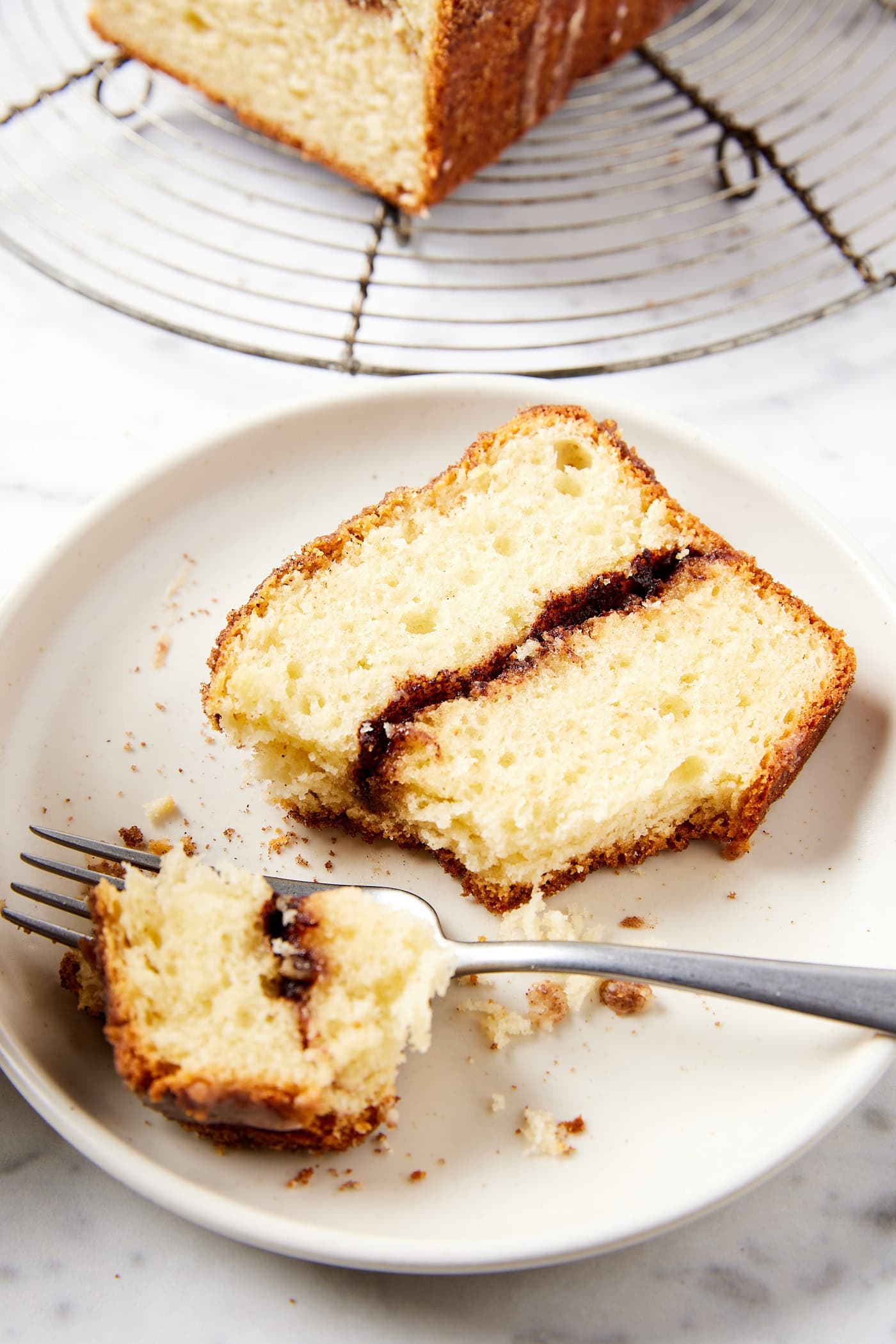 White plate with slice of sour cream coffee cake with fork taking a piece showing interior crumb texture.