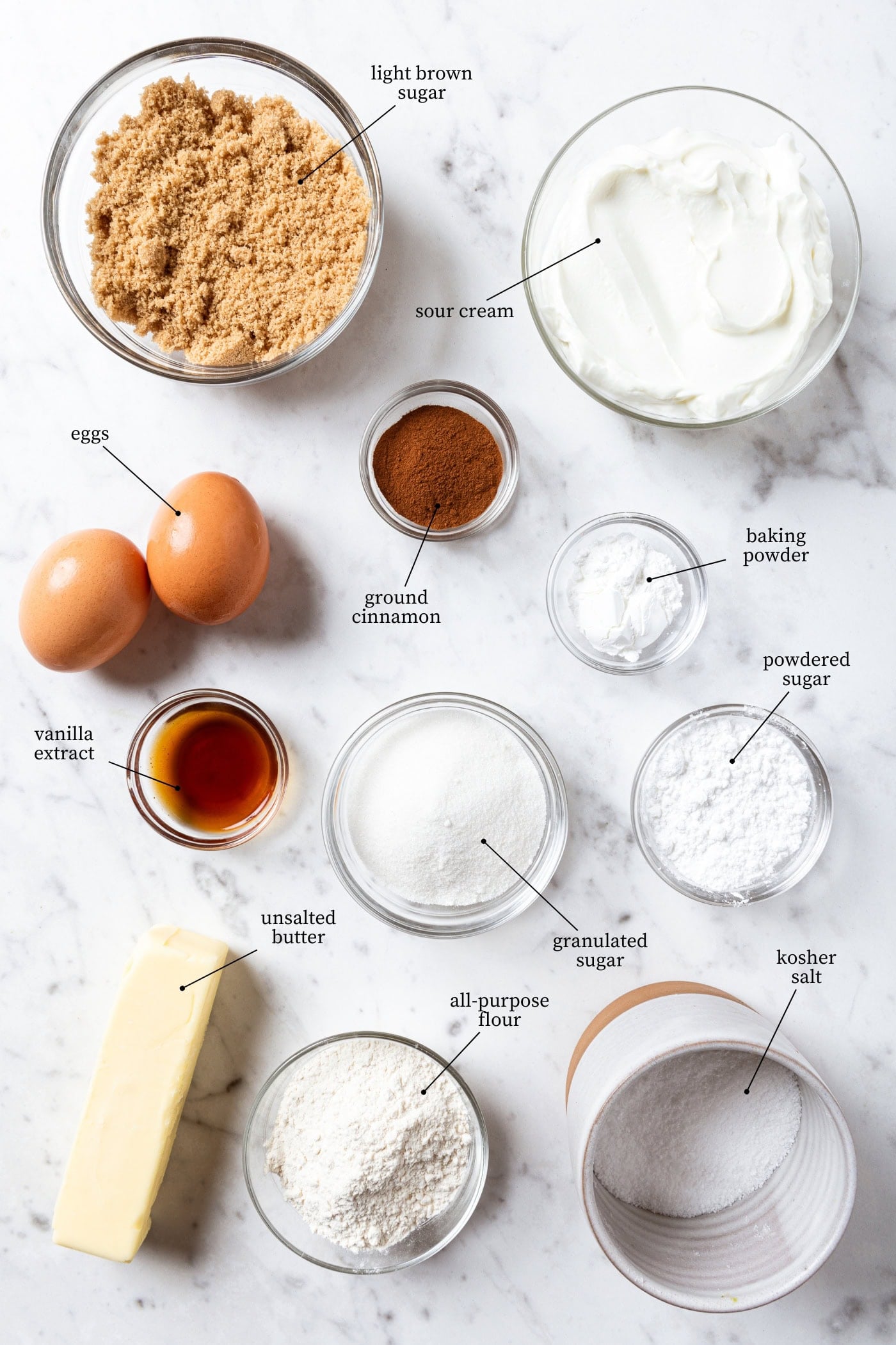 White marble surface filled with ingredients needed for coffee cake including sugar, brown sugar, flour, butter, and more.