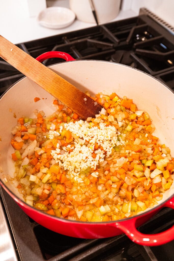 Garlic added to aromatics in a Dutch oven.