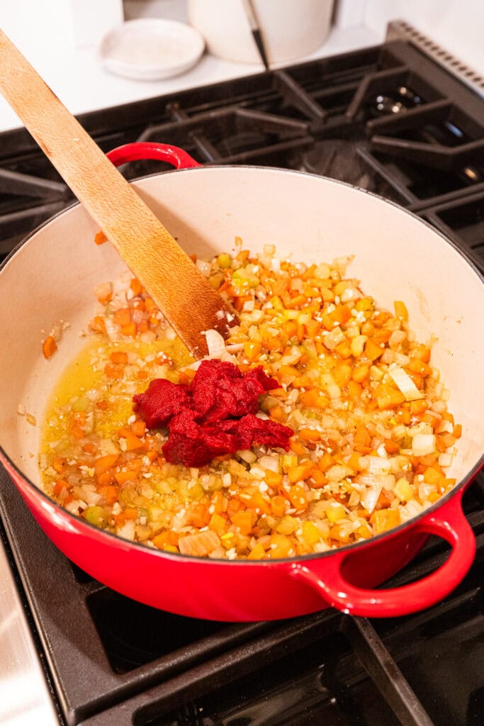 Tomato paste added to vegetables in a Dutch oven.