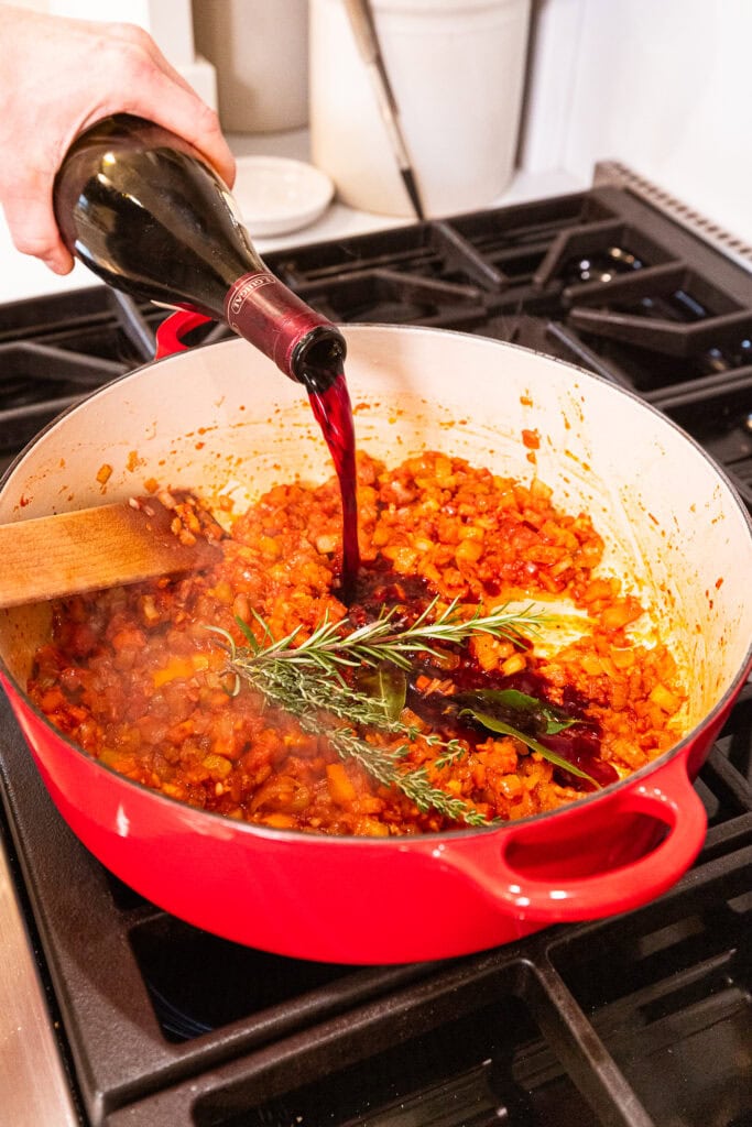 Adding wine to aromatics in a Dutch oven.