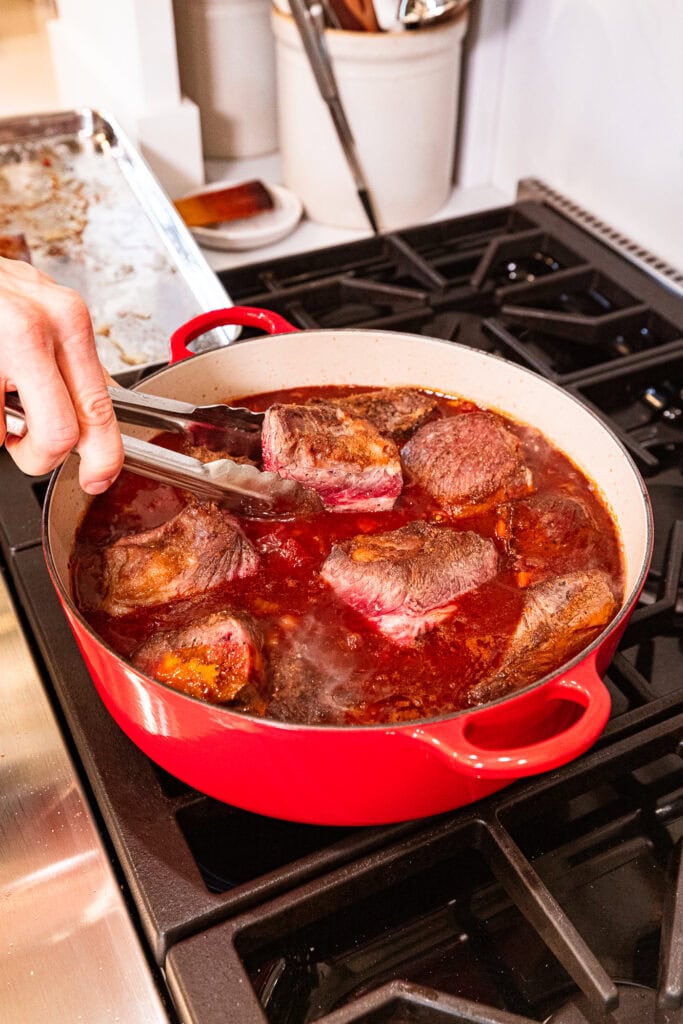 Adding short ribs to a sauce over heat.