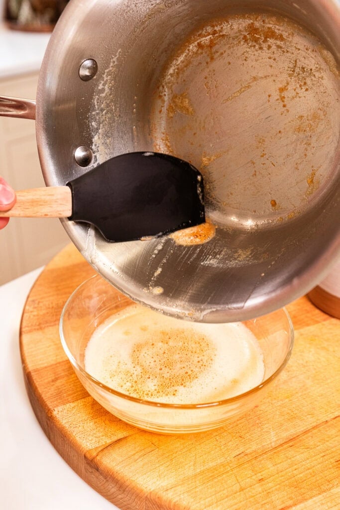 Pouring brown butter from a saucepan into a bowl to cool.