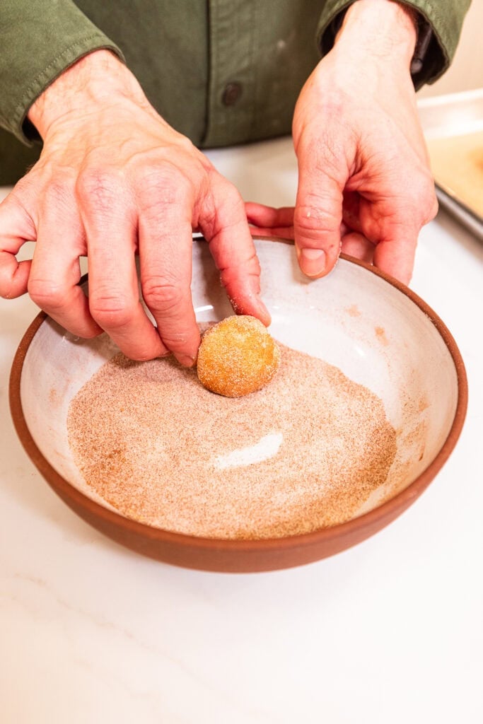 Rolling balls of snickerdoodle cookie dough in a spice mix prior to baking.
