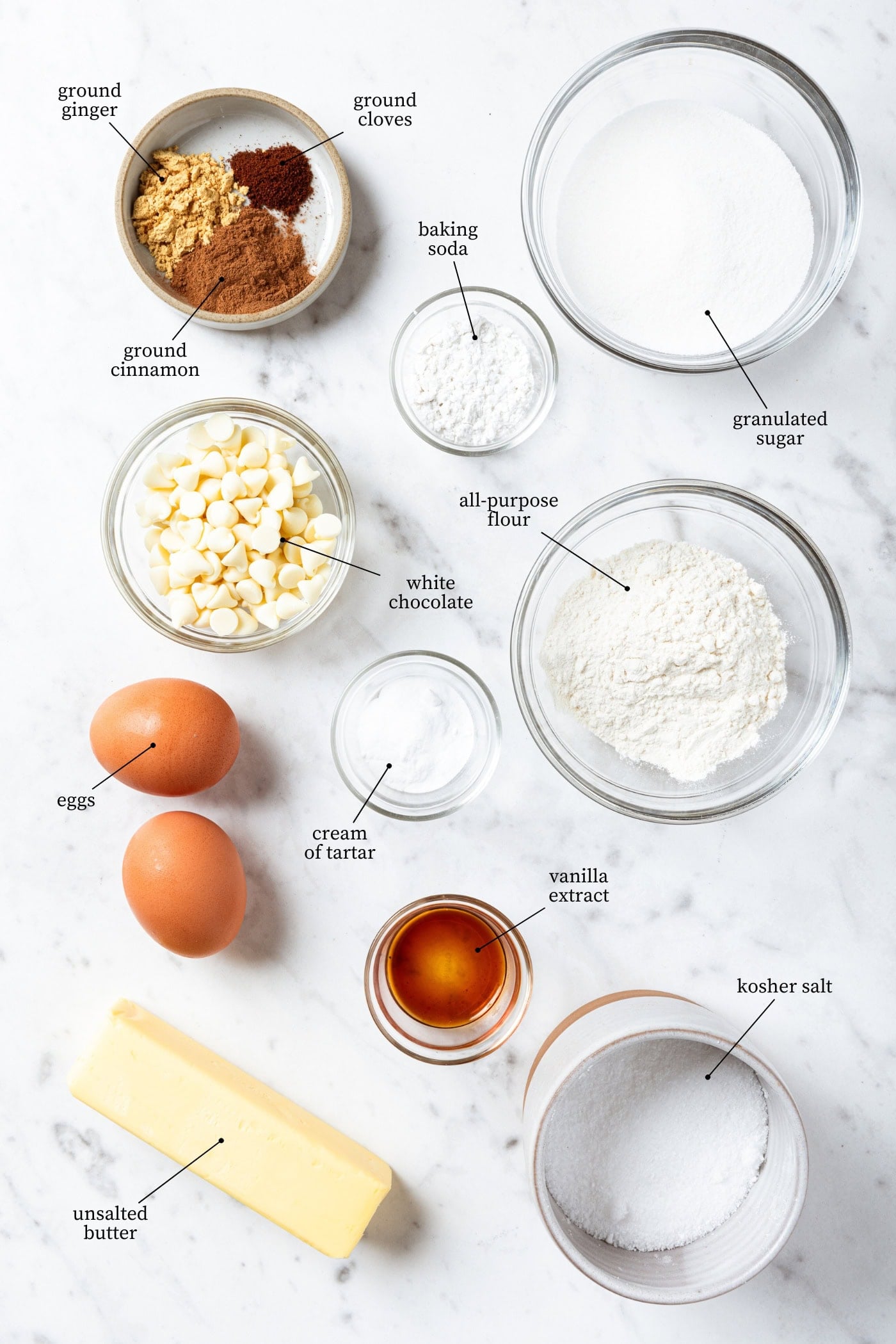 White marble surface filled with all ingredients needed to make snickerdoodle cookies including flour, sugar, eggs, vanilla, butter, and more.