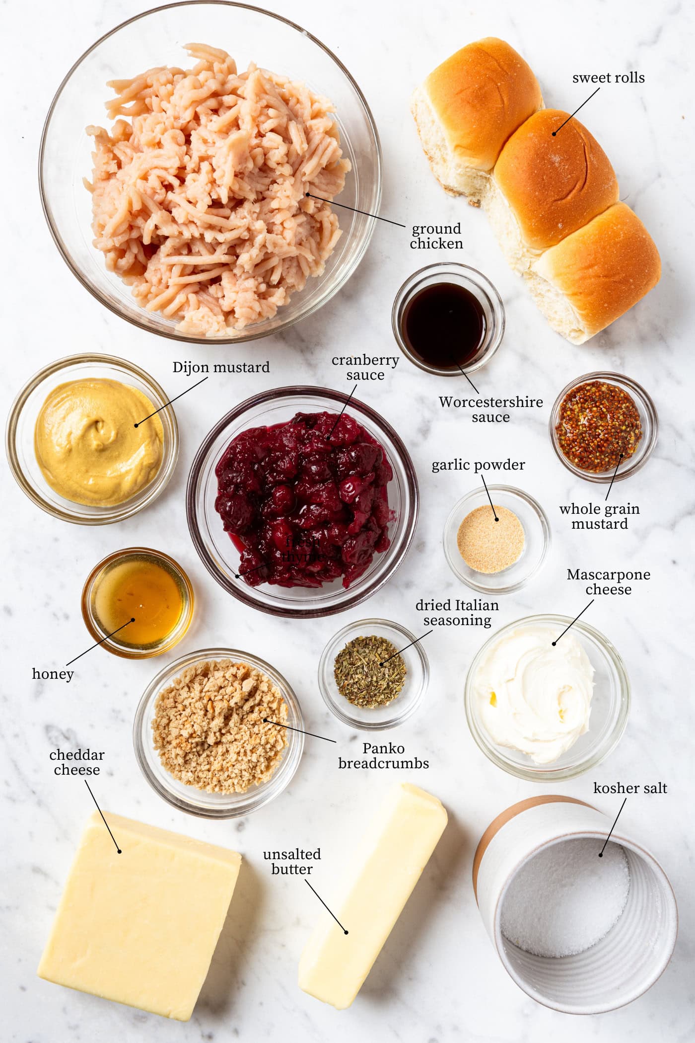 White marble surface filled with ingredients for cranberry chicken meatball sliders including ground chicken, cranberry sauce, spices, and more.