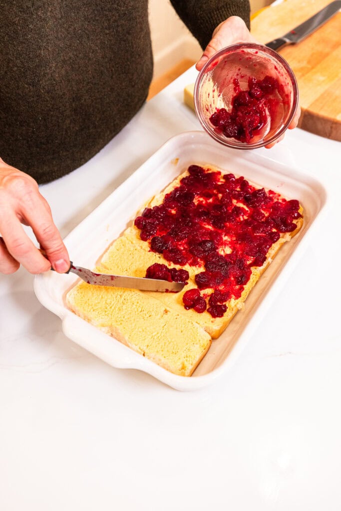 Spreading cranberry sauce over the bottom half of sweet rolls in a baking dish.