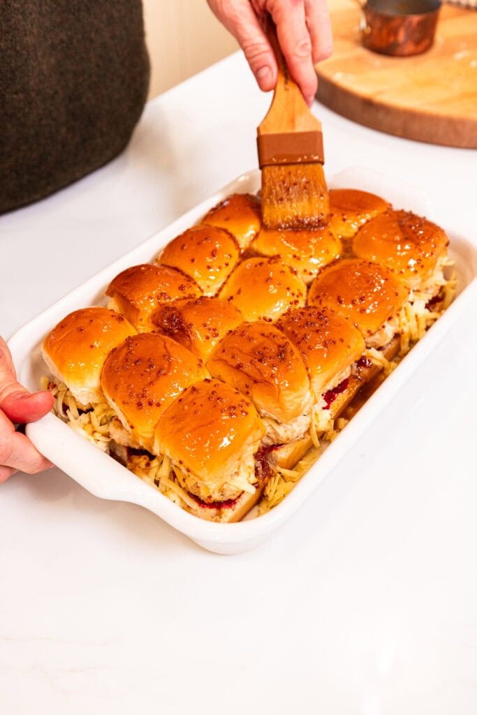 Spreading a butter mixture over the tops of sliders in a baking dish.
