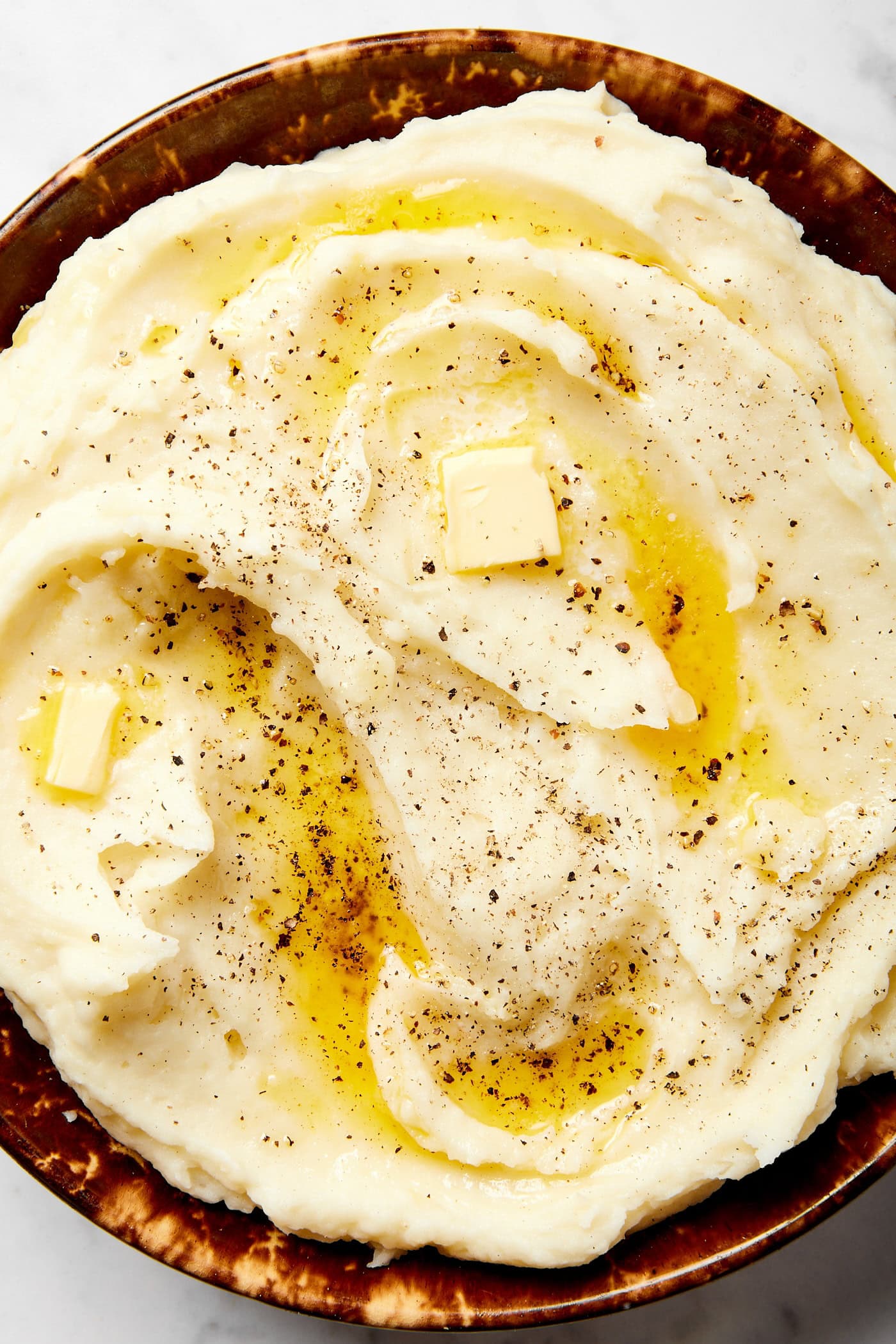 Pieces of butter melting on top of mashed potatoes with sprinkling of black pepper.