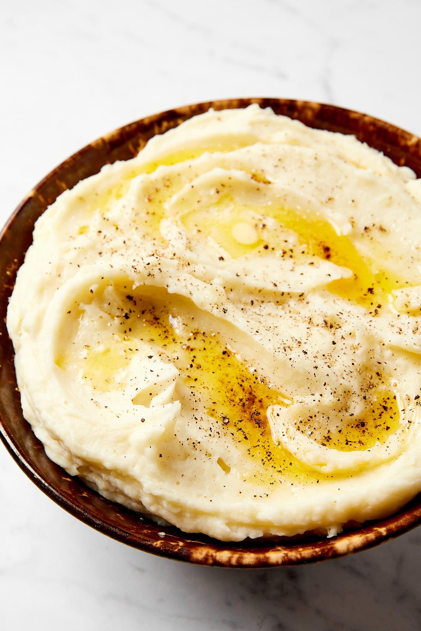 Large brown bowl filled with buttery mashed potatoes with black pepper sprinkled on top.