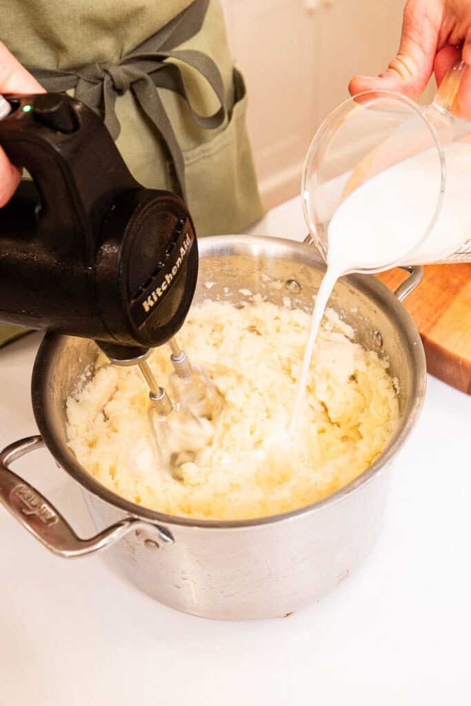 Adding whole milk to mixed potatoes.