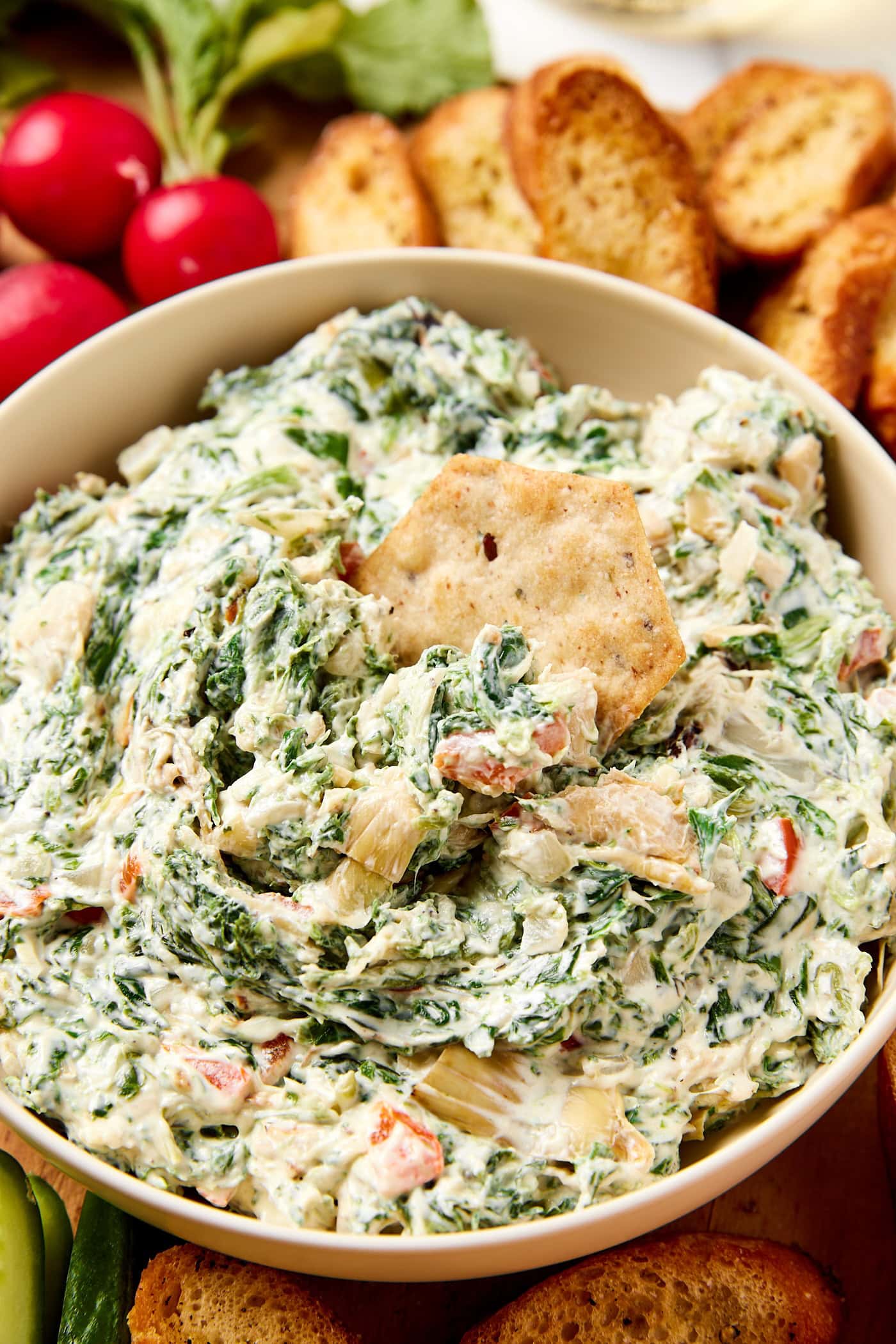 Chip stuck in a bowl filled with spinach artichoke dip with flecks of spinach and red bell pepper.