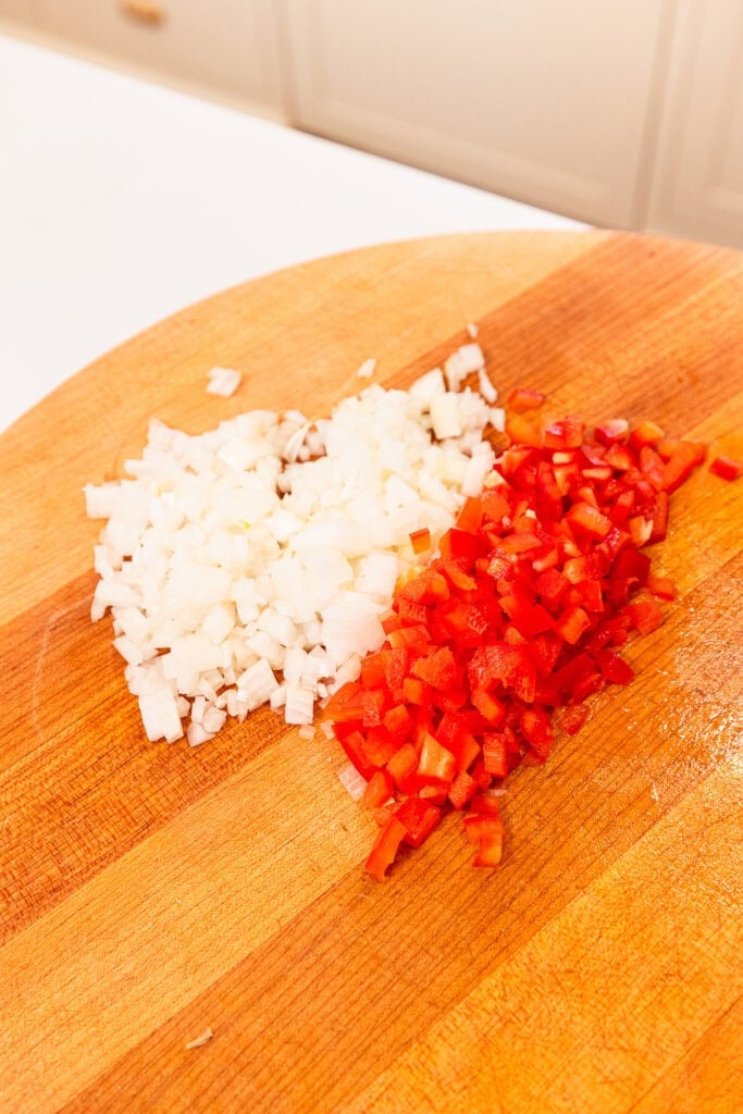 Diced onions and red bell peppers on a chopping block.