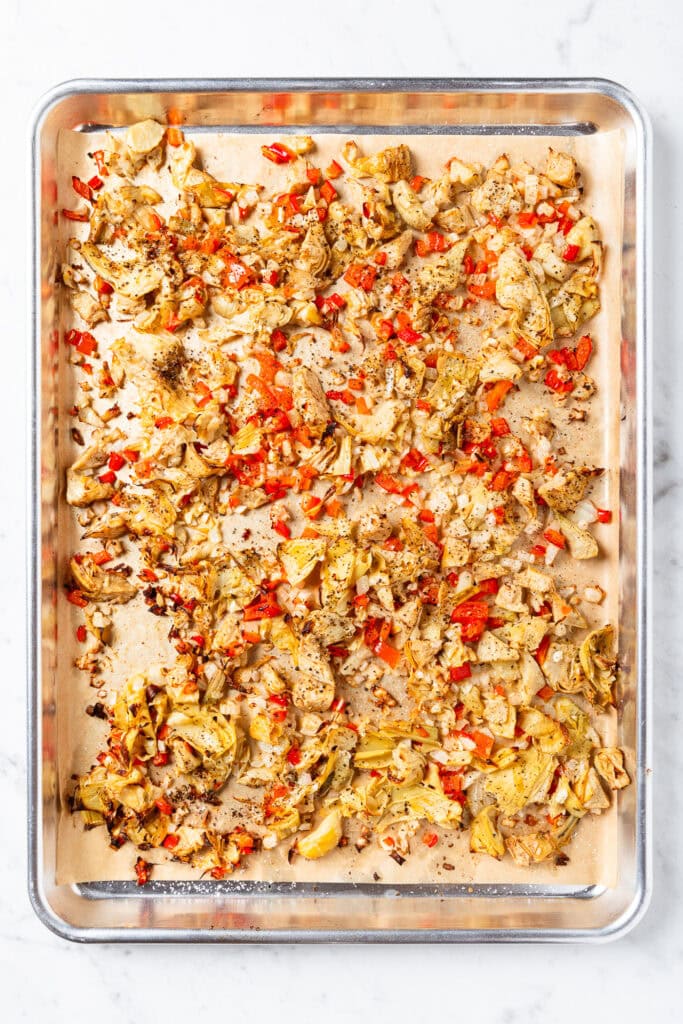Artichoke hearts, onions, and peppers on a pan after roasting.