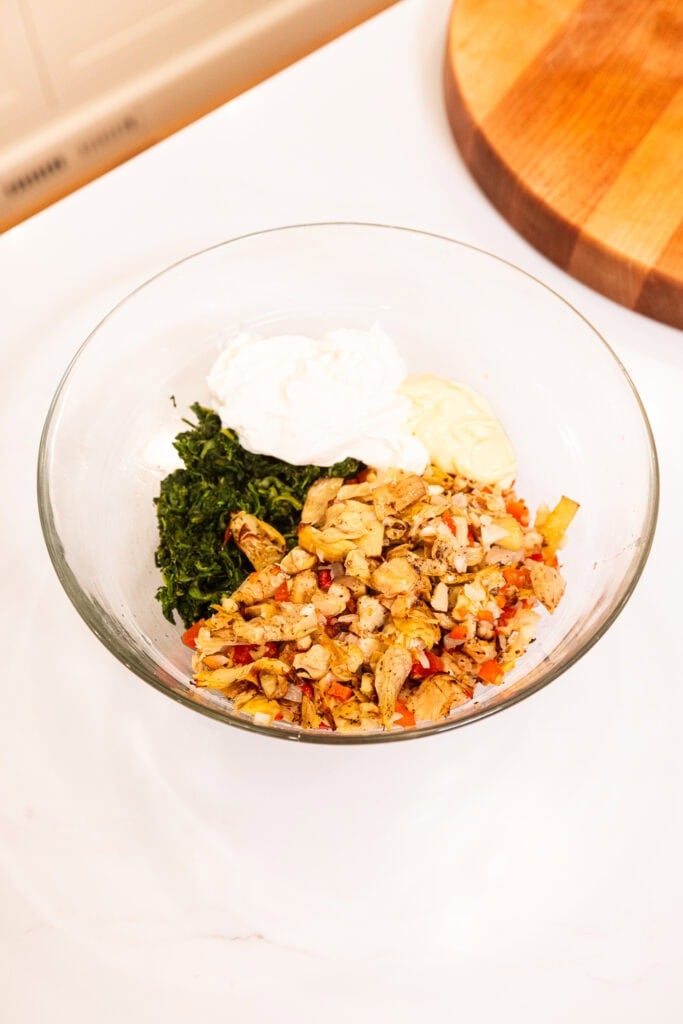 Ingredients to create spinach artichoke dip sit in a bowl before being combined.