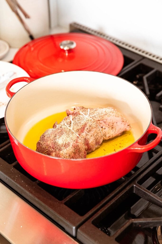 Pork roast browns over a stove in a Dutch oven.