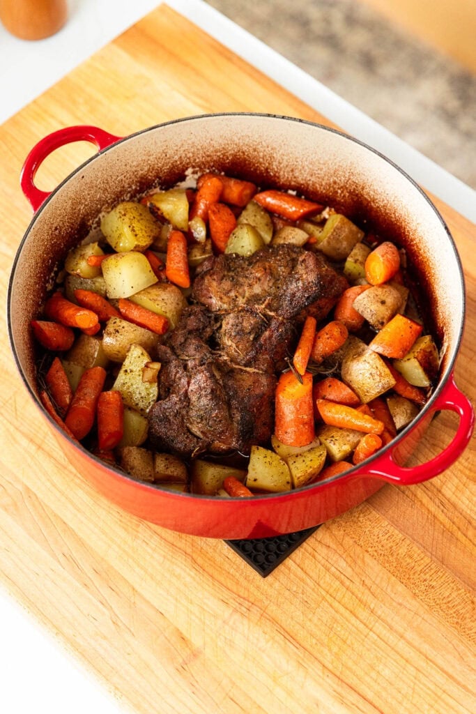 Pork roast with vegetables sits in a pot on a cutting board.