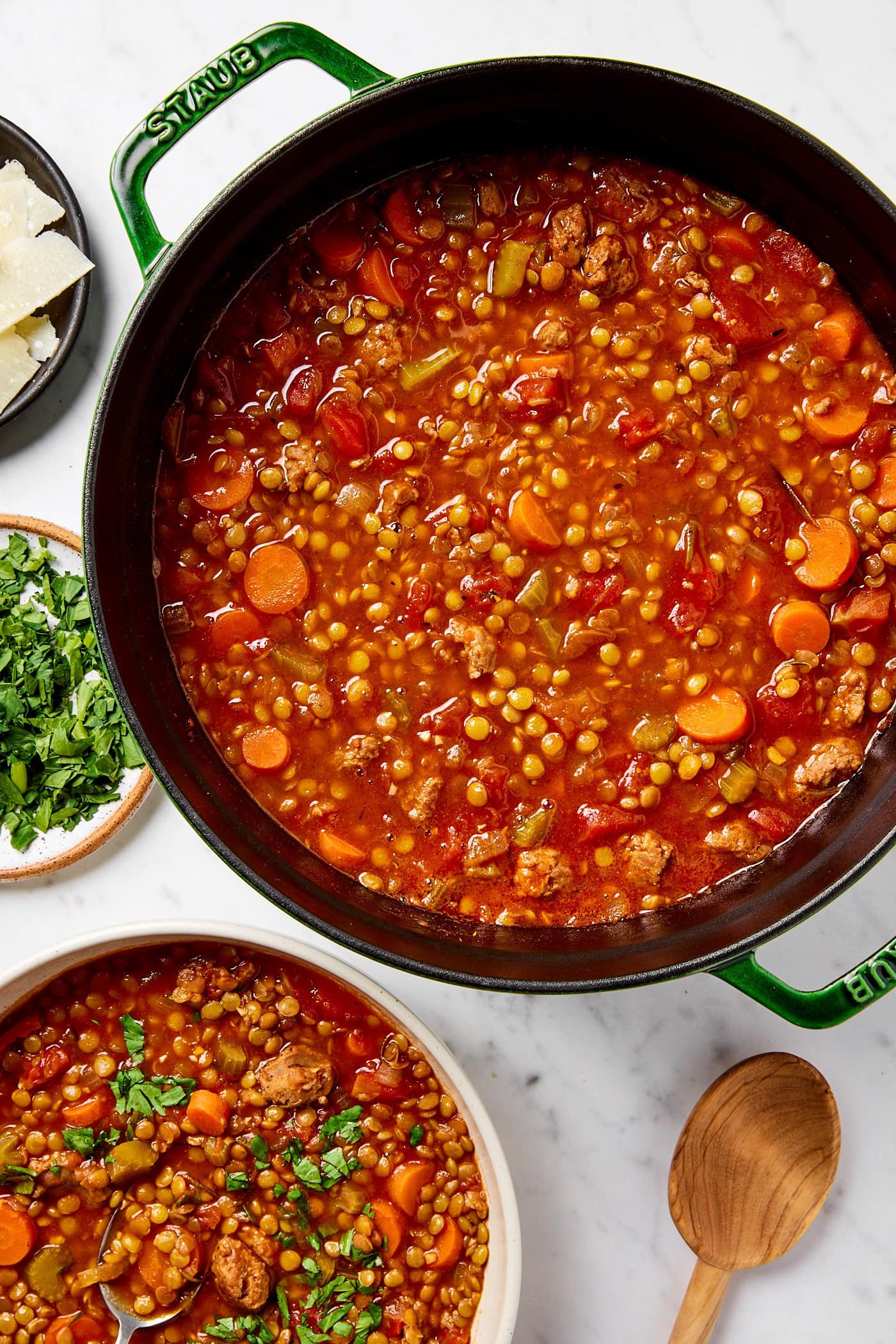 Sausage and lentil soup in a bowl sitting next to a pot full of the same soup.