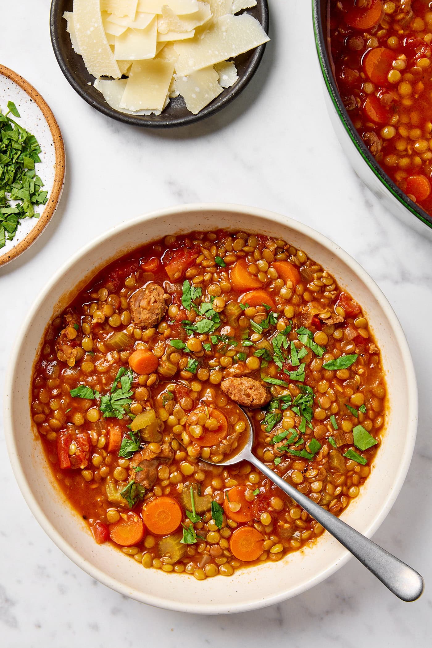 A bowl full of sausage and lentil soup garnished with parsley.