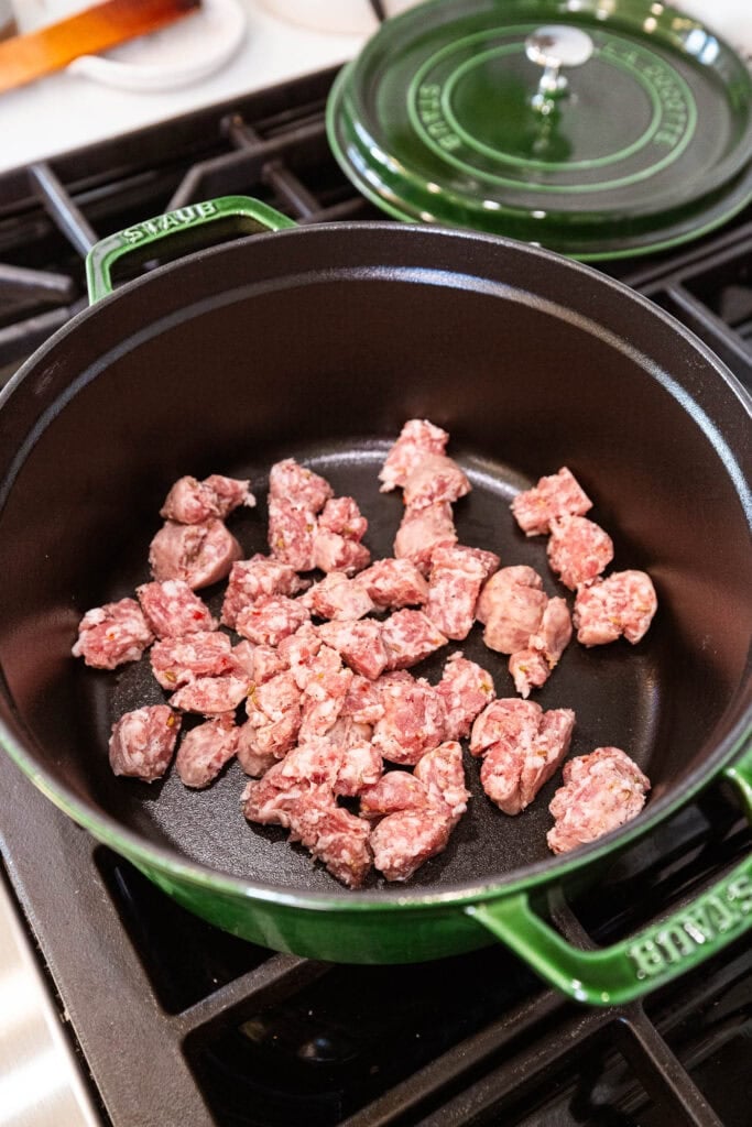 Raw sausage in a Dutch oven begins to brown over heat.
