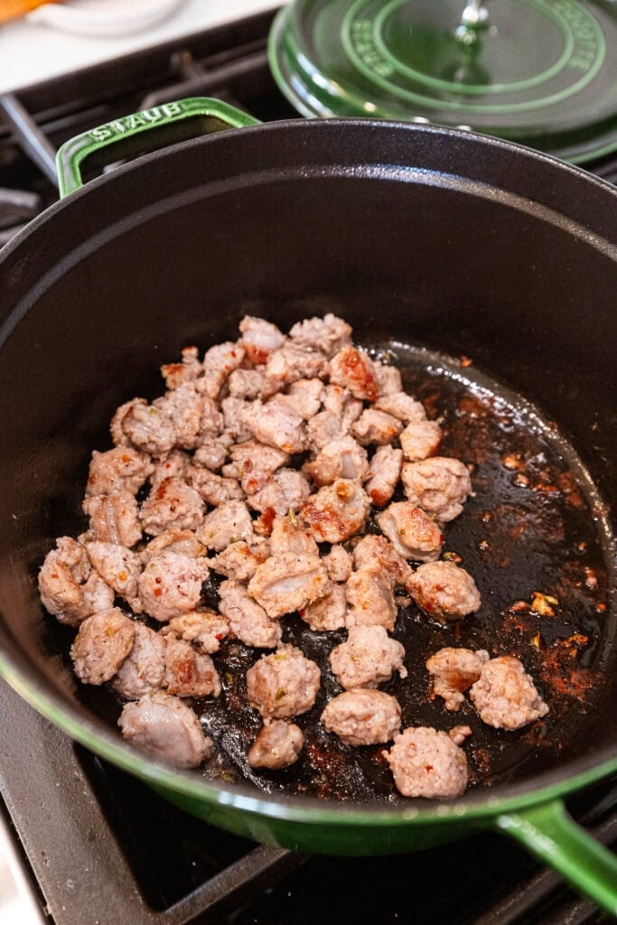 Browned sausage in a Dutch oven on the stove.