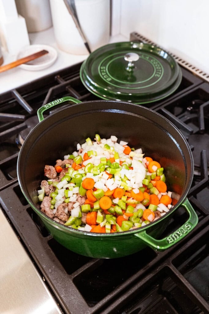 Carrot, celery, and onion cook with sausage in a Dutch oven.
