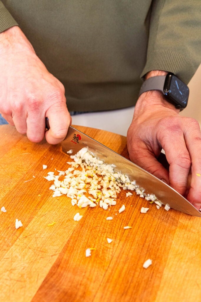 Mincing garlic on a cutting board.