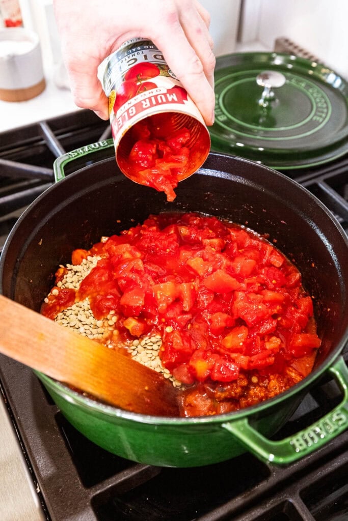 Adding diced tomatoes to lentils to form soup.