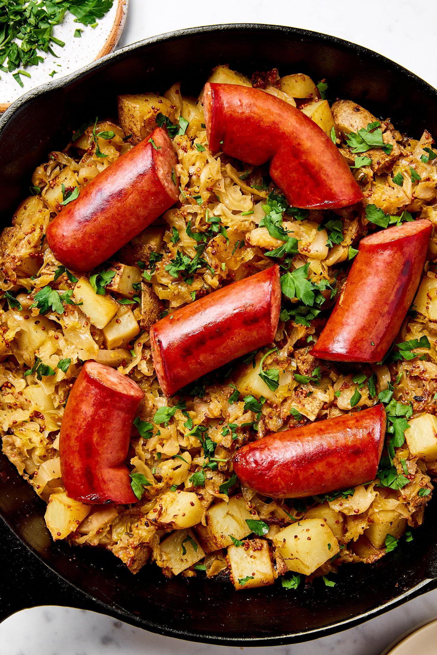 Kielbasa in an iron skillet with sauerkraut, potatoes, and onion.