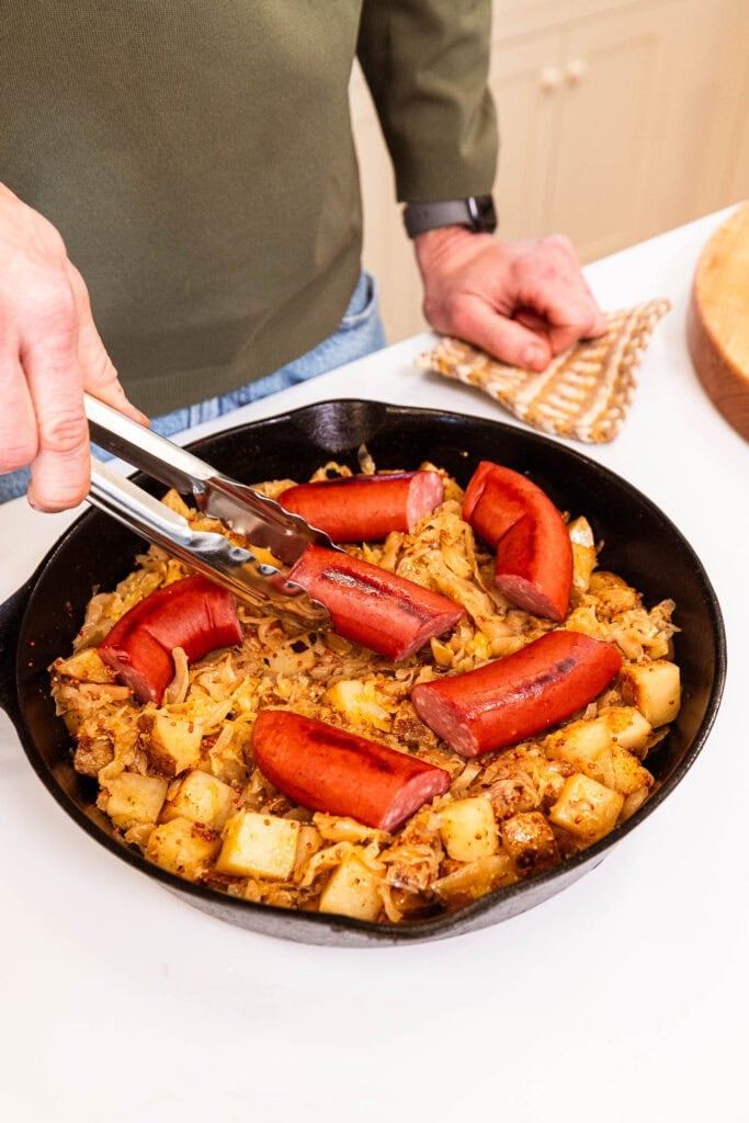 Placing kielbasa overtop sauerkraut and potatoes after roasting.