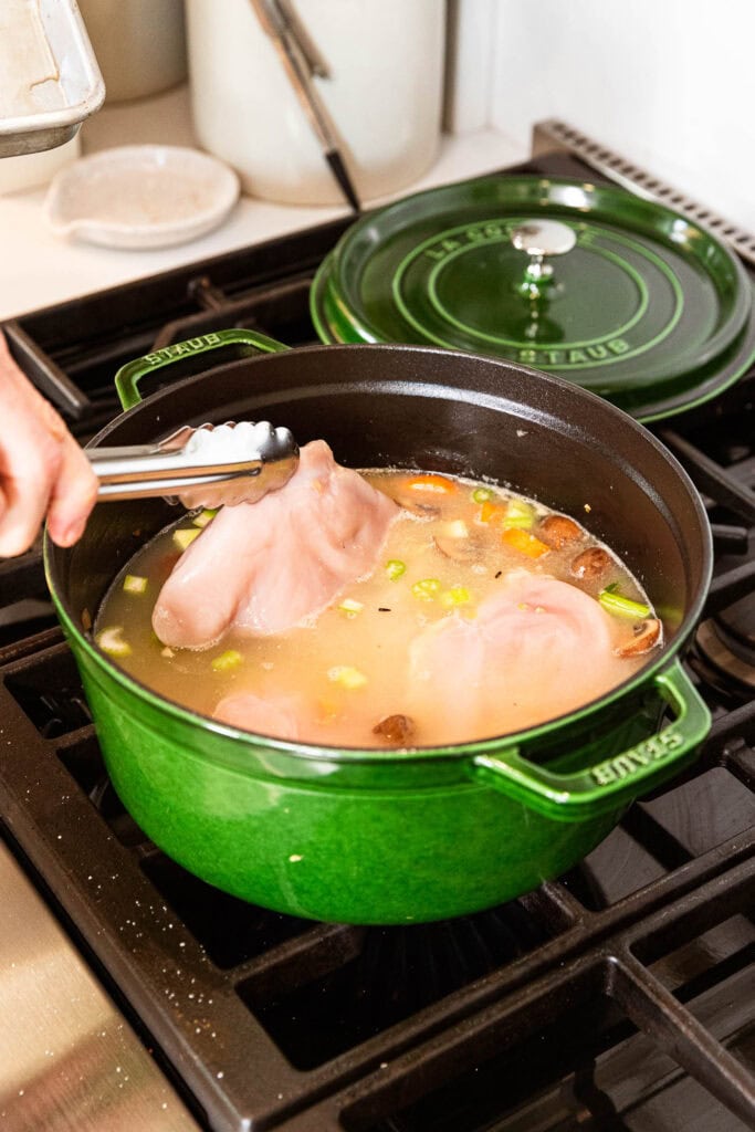 Placing chicken breast into stock to poach.