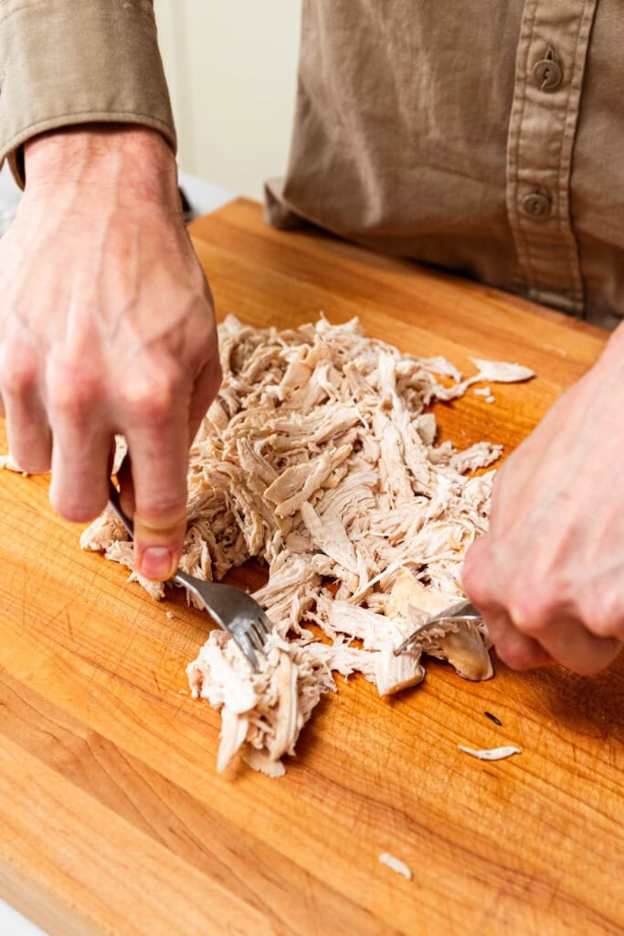 Shredding chicken by hand on a cutting board.