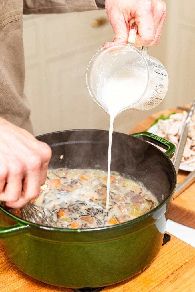 Adding whole milk and flour mixture to thicken soup in a pot.