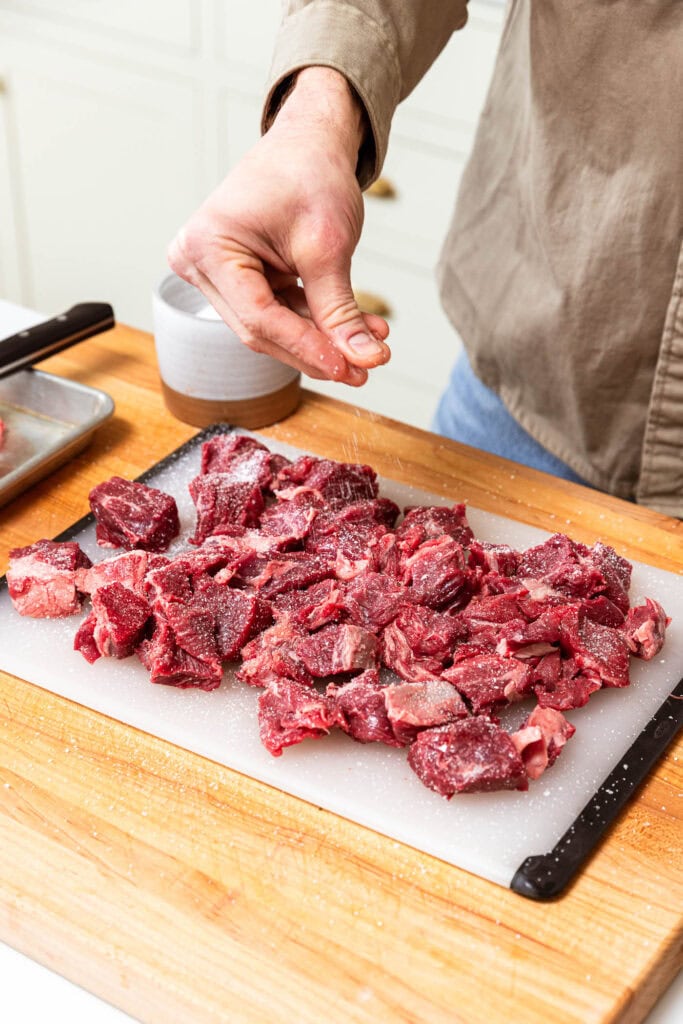 Seasoning cubes of chuck roast with salt.