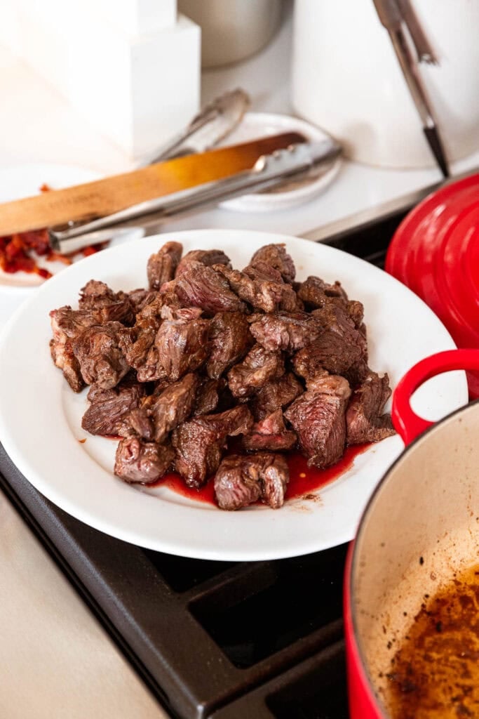 Browned cubes of beef rest on a plate after an initial cook.