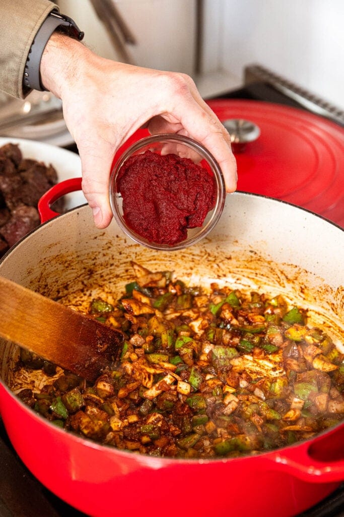 Adding tomato paste to chopped vegetables sautéing in a pot.
