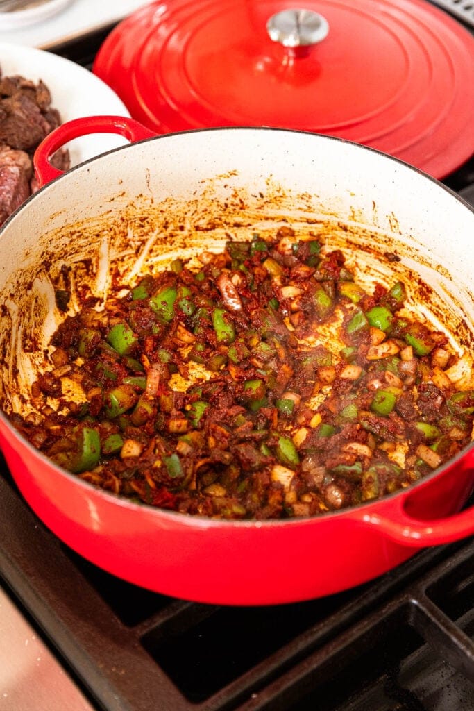 Diced vegetables and tomato paste cook in a pot.