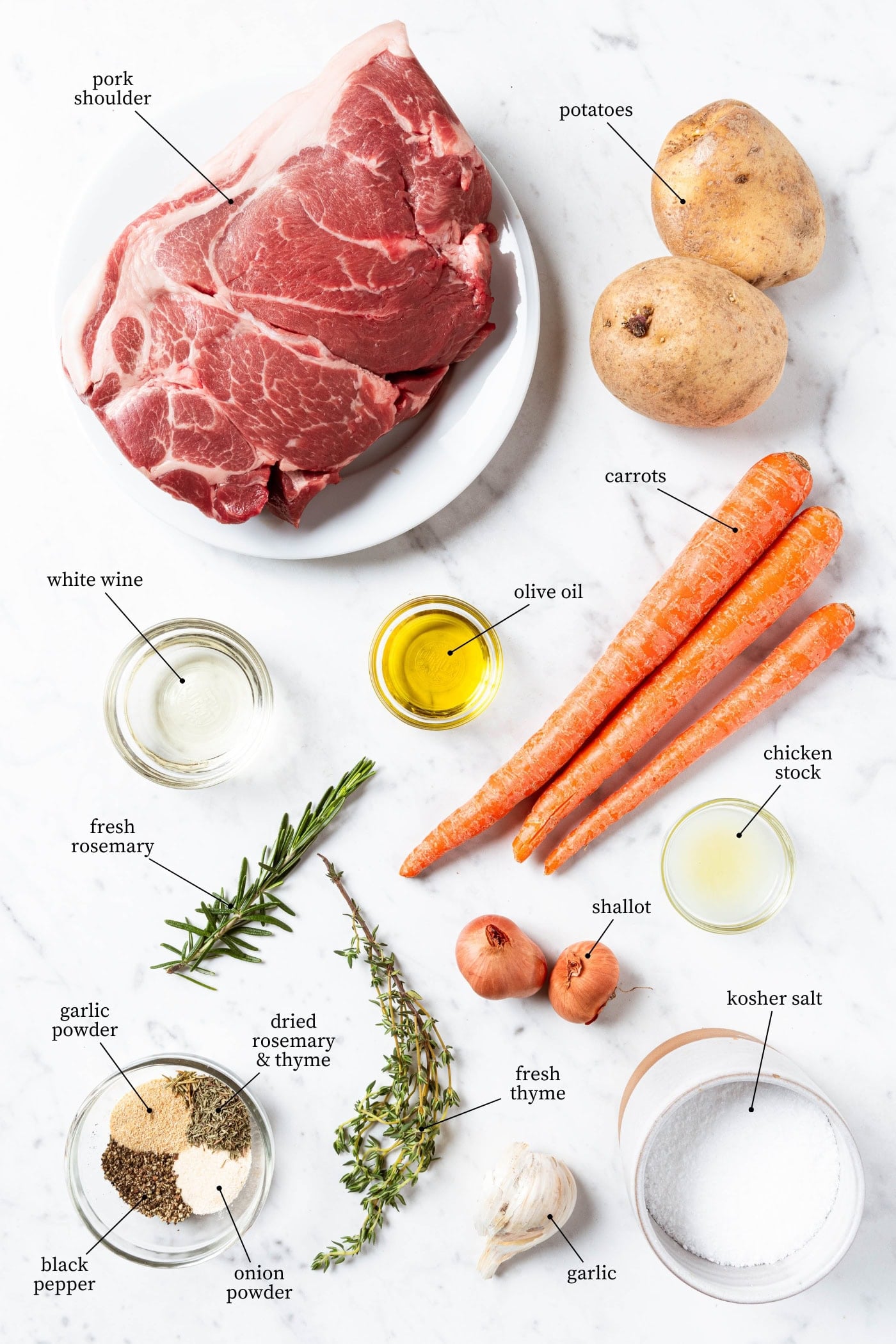 White marble surface filled with ingredients needed for pork pot roast including pork shoulder, spices, wine, carrots, potatoes, and more.