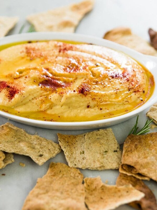 Rosemary homemade crackers broken into pieces with a bowl of hummus in the background.
