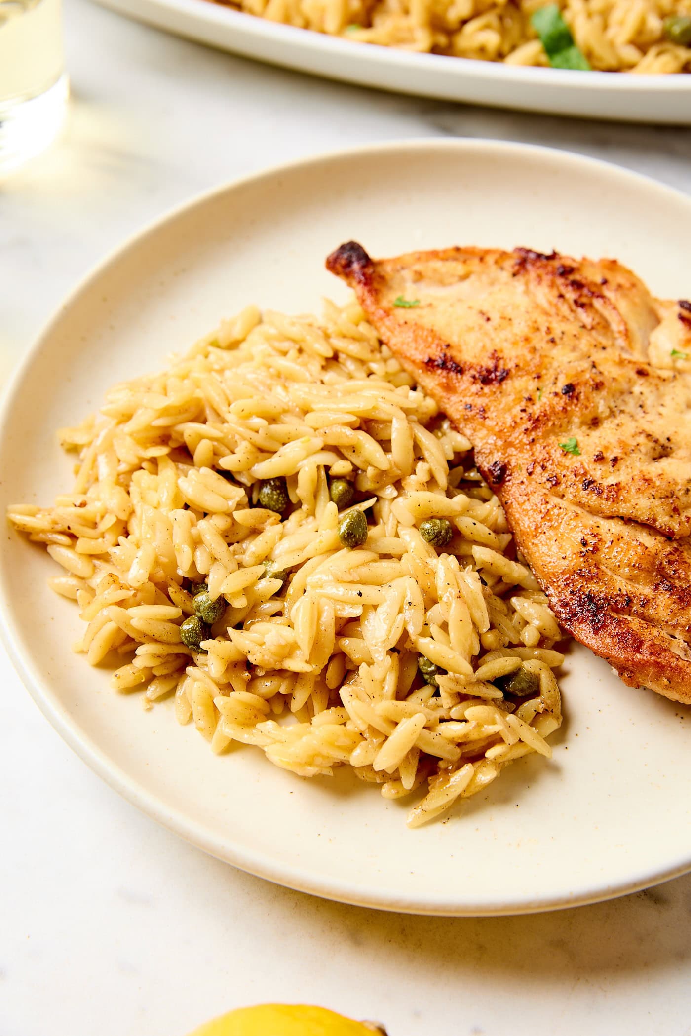 Creamy orzo with capers next to chicken breasts.