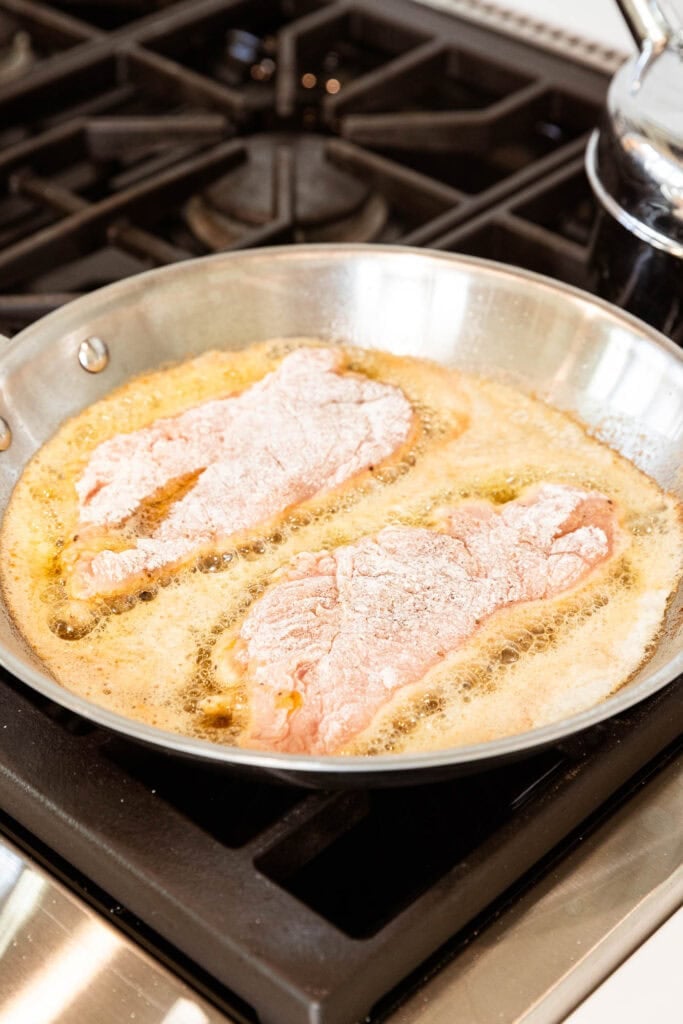 Chicken cutlets cooking over a stove.