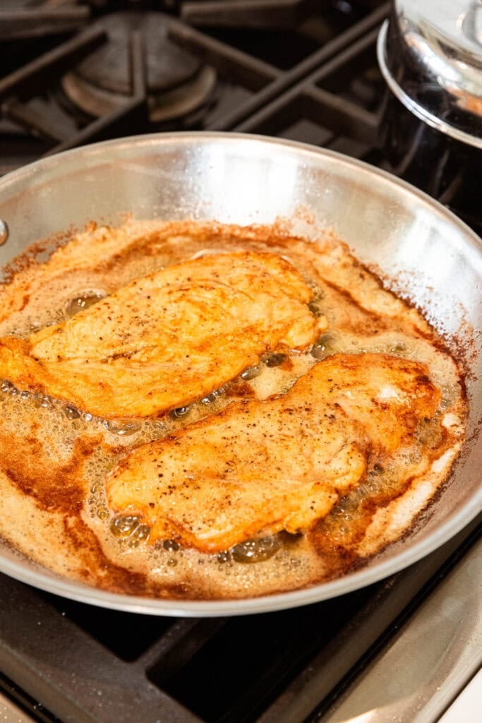 Chicken breast cooking in butter and oil on the stove.