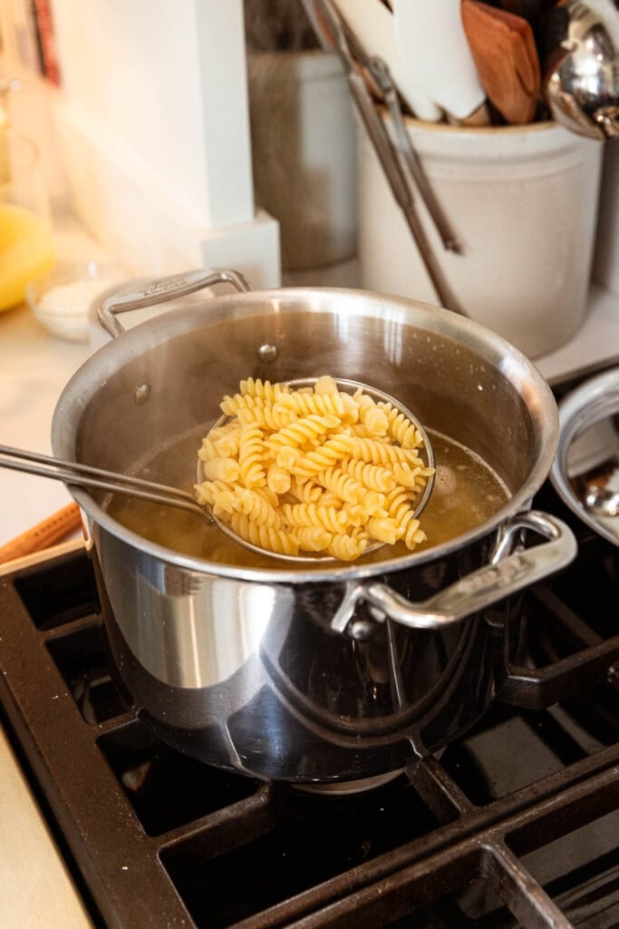 Scooping out pasta noodles after they have cooked in a pot.