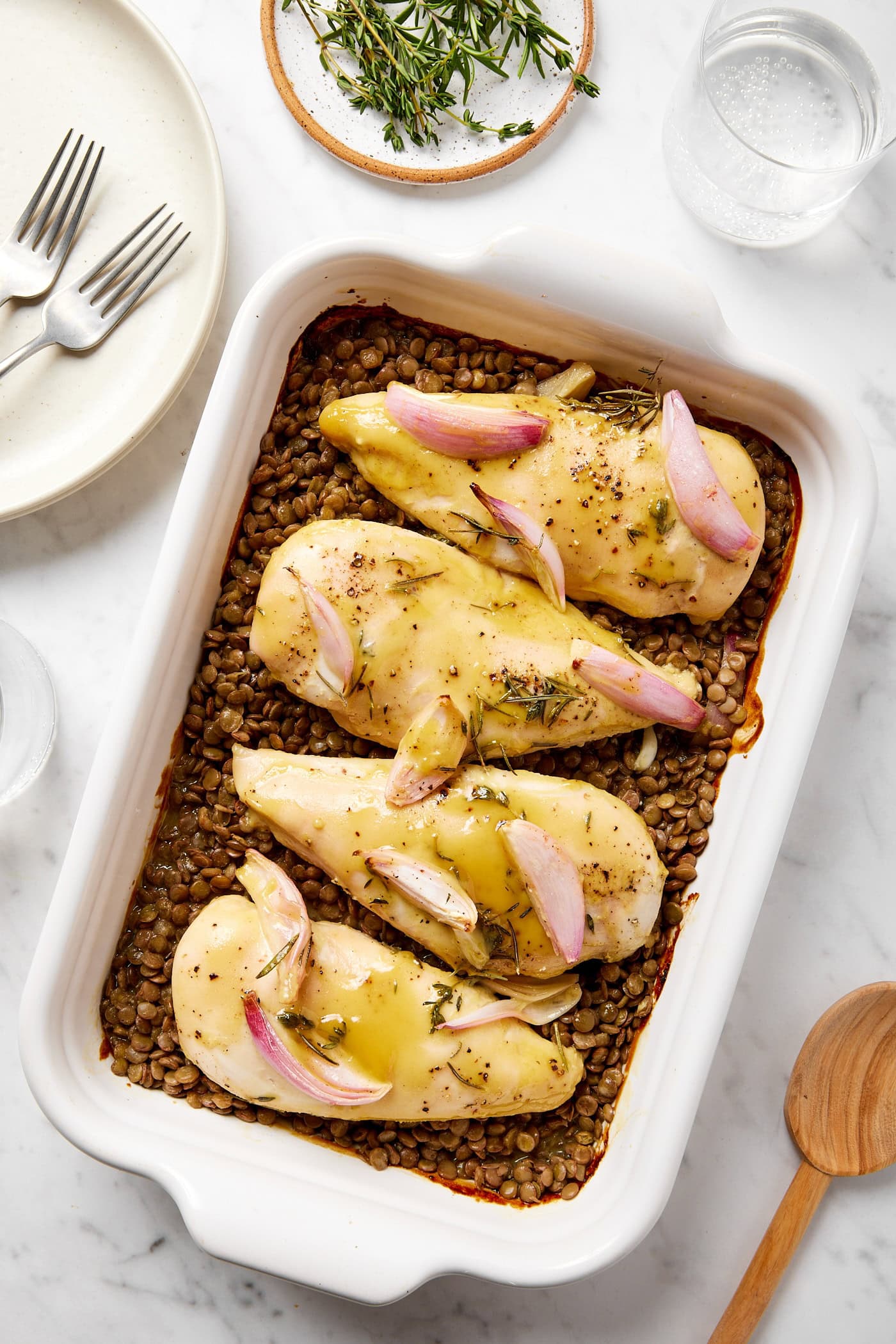 Chicken breasts sit on top of lentils in a baking dish.