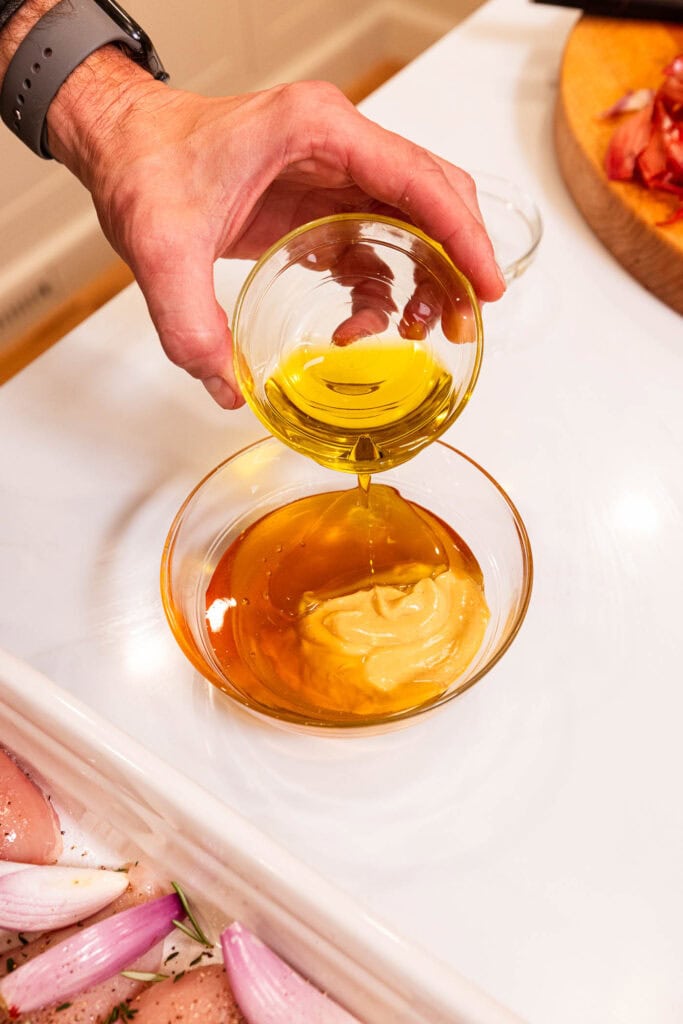 Adding olive oil to Dijon mustard and honey to make a marinade.