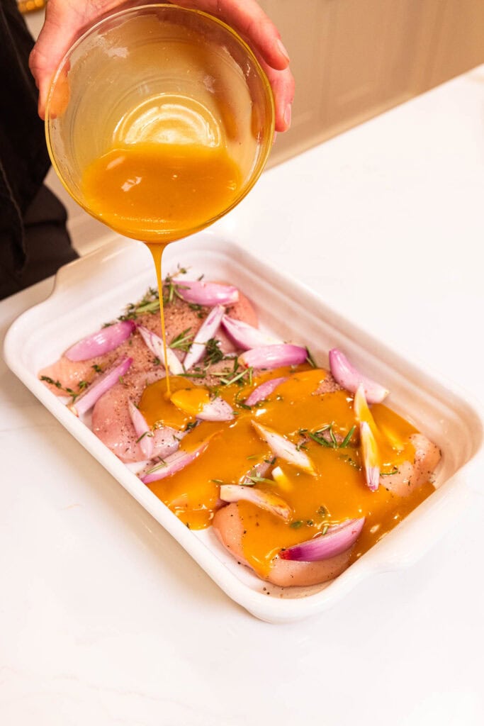Pouring honey mustard marinade over chicken breasts.