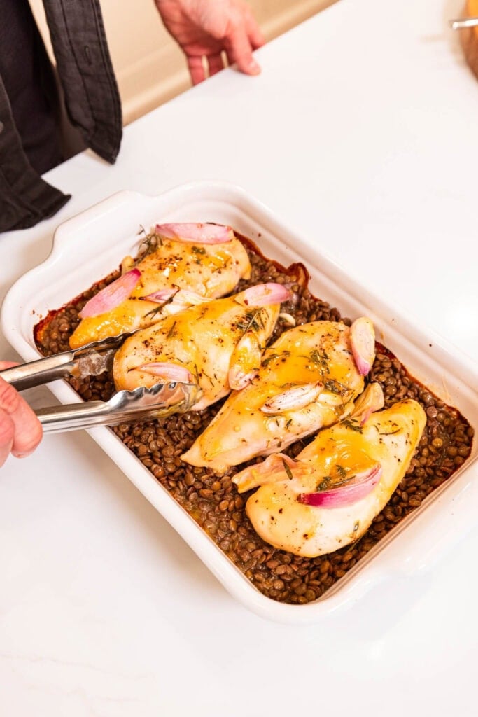 Nestling honey mustard chicken breasts over lentils in a baking dish.