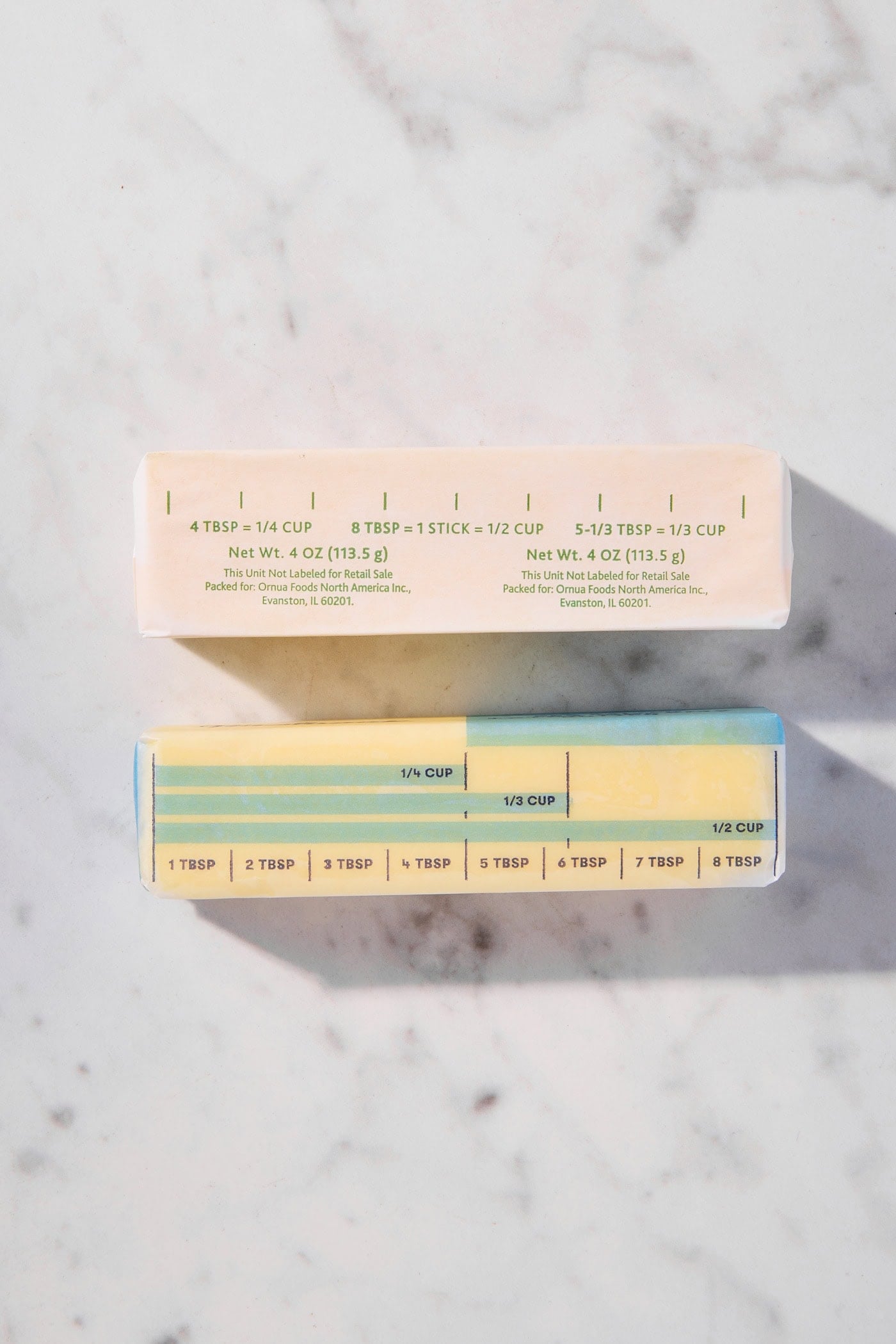 Sticks of butter on piece of marble with their paper still on.