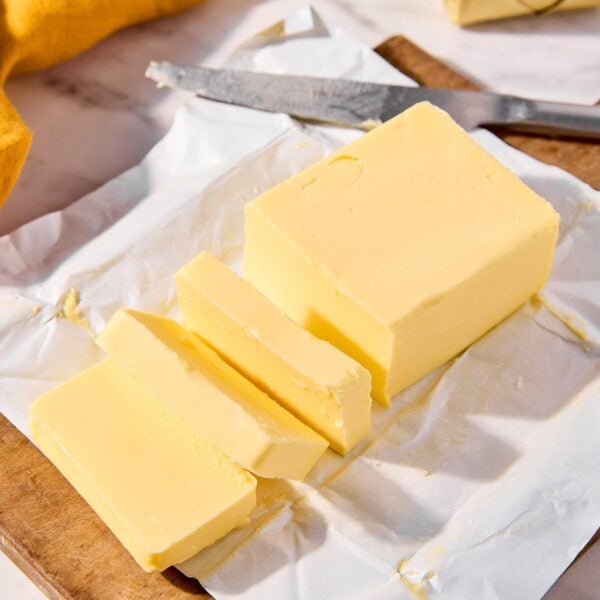 Large stick of butter sliced into pieces sitting on it's wrapping paper.