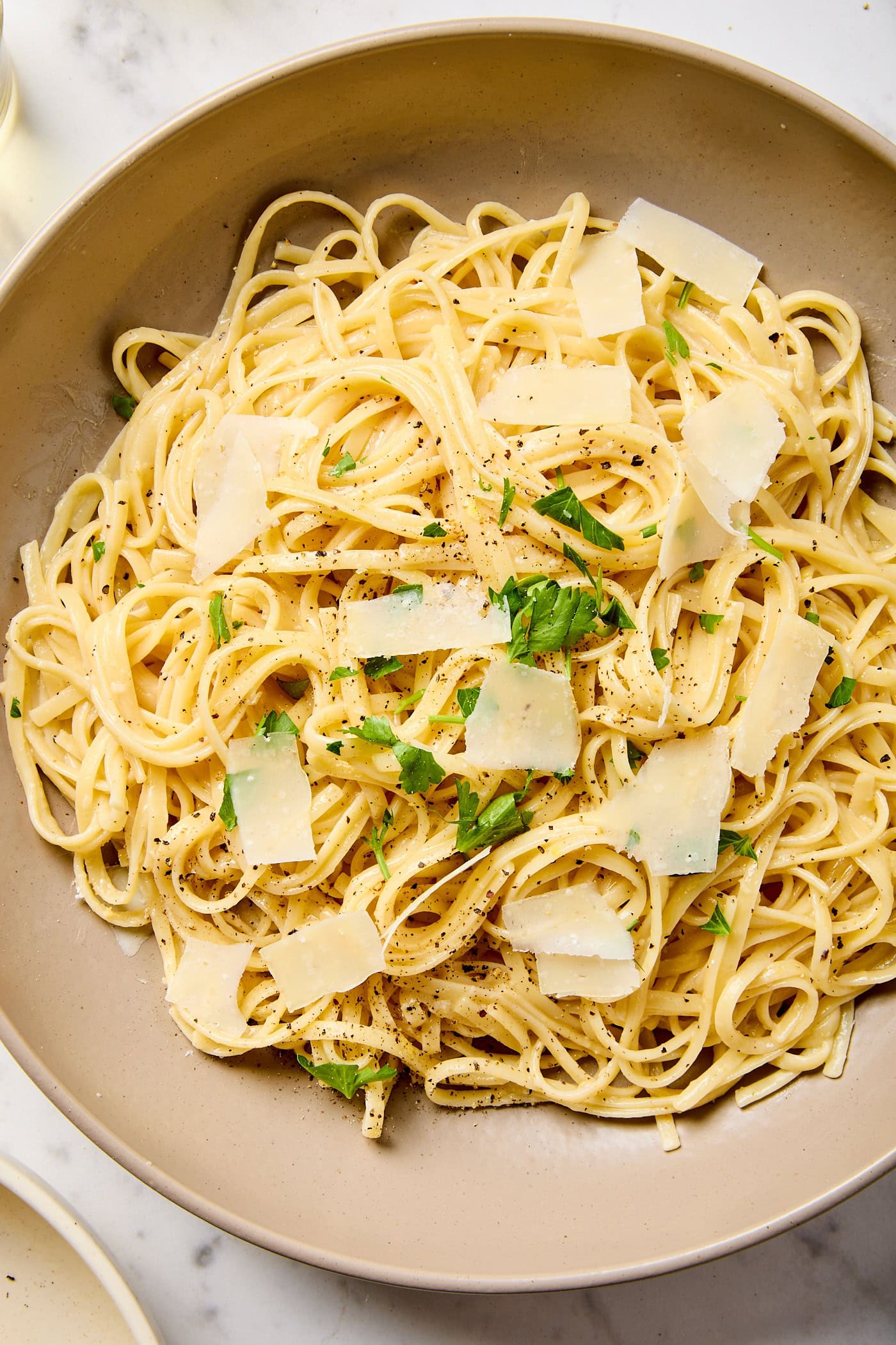 A bowl full of lemon butter pasta topped with parsley and Parmesan shavings.